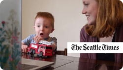 Child playing with a red train while a woman looks at him smiling. The Seattle Times.